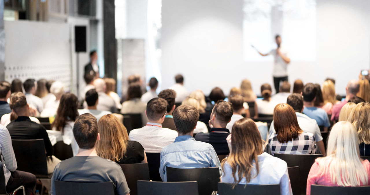 Speaker giving a talk in conference hall at business event. Audience at the conference hall. Business and Entrepreneurship concept. Focus on unrecognizable people in audience.