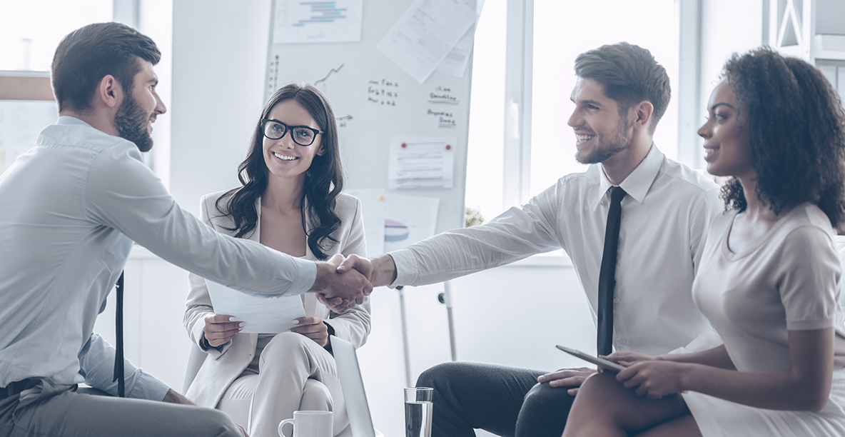 Office meeting between two smiling men shacking their hands and two smiling women