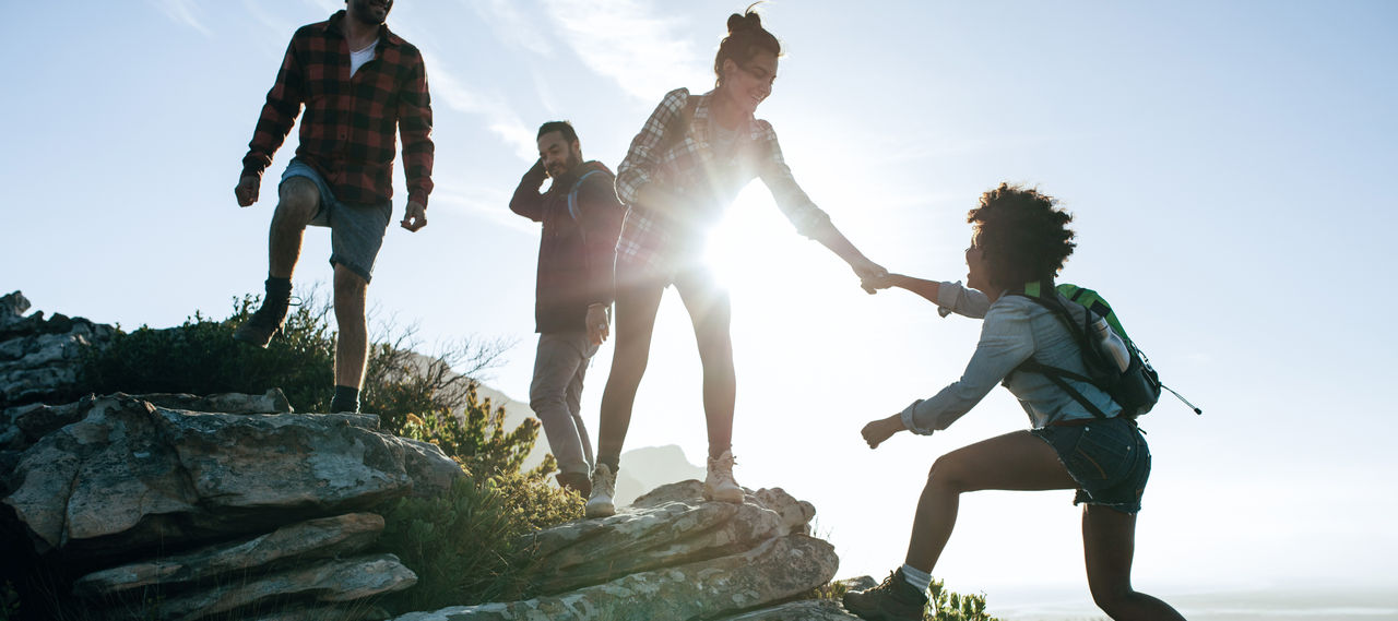 Group of hikers on a mountain. Woman helping her friend to climb a rock. Young people on mountain hike at sunset.